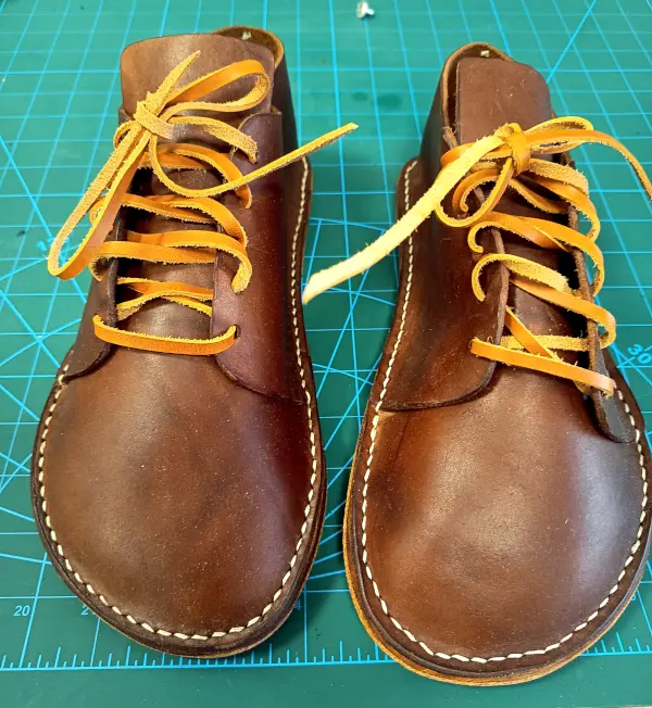 Detail ruční práce na hnědých botách na ševcovské podložce