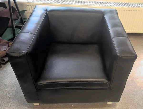 Renovace moderního křesla natažením nové černé kůže, ruční práce čalouníka.