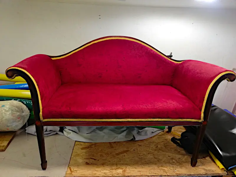 Zrenovovaná historická pohovka s červeným potahem a zlatým lemem